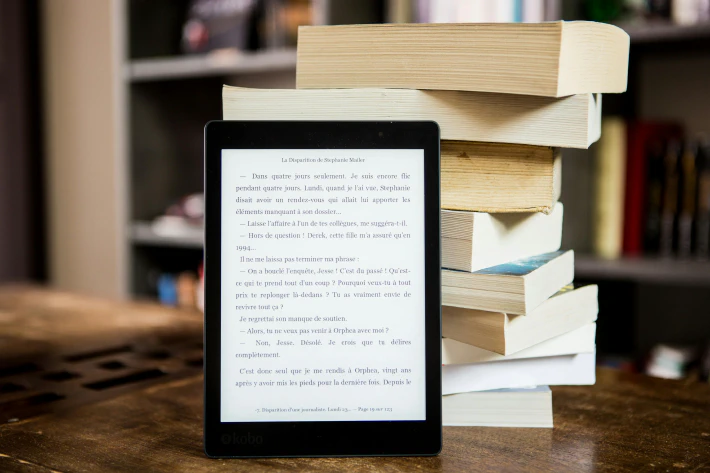 An e-reader tablet in front of a stack of books 